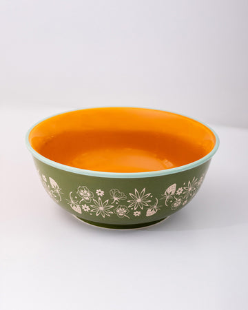 side view of green small ceramic serving bowl with orange interior and red strawberry stamp inside and light blue trim