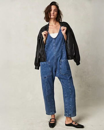 model wearing dark wash relaxed fit jumpsuit with front seaming and front patch pockets, white tube top and leather jacket