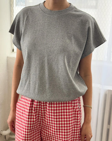 model wearing heather grey tee with slight cap sleeves, relaxed fit, and banded bottom