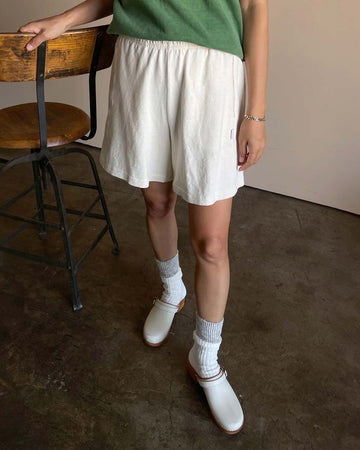 model wearing cream colored cotton basketball shorts with side pockets and slits on the side