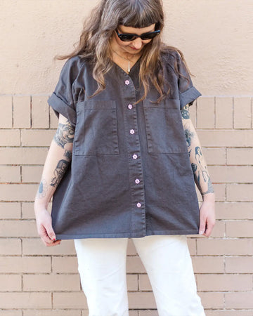 model wearing grey relaxed fit button front top with 2 large patch pockets on the bust and pink flower shaped buttons