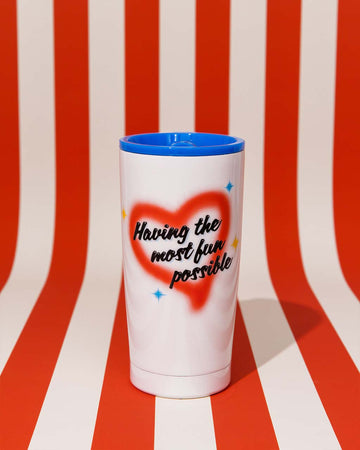 white stainless steel mug with air sprayed 'having the most fun possible' and blue lid on red and white stripe background