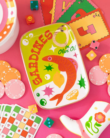 editorial image of trinket tray that looks like a sardine can surrounded by colorful items